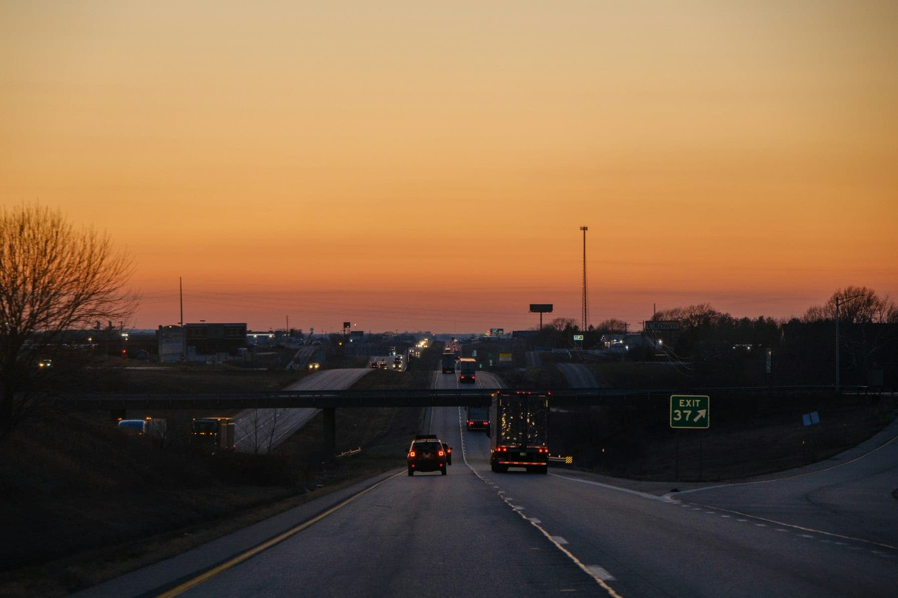Interstate highway at dusk under a glowing amber sky with a semi truck heading toward an overpass