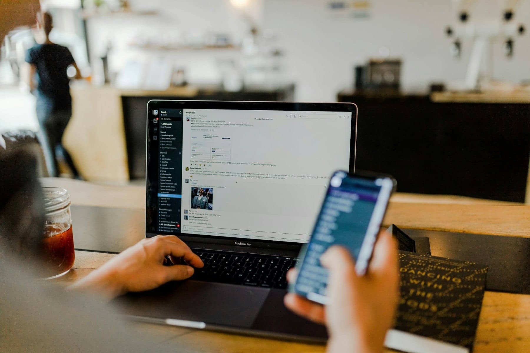 Hands typing on a laptop while holding a smartphone at a desk
