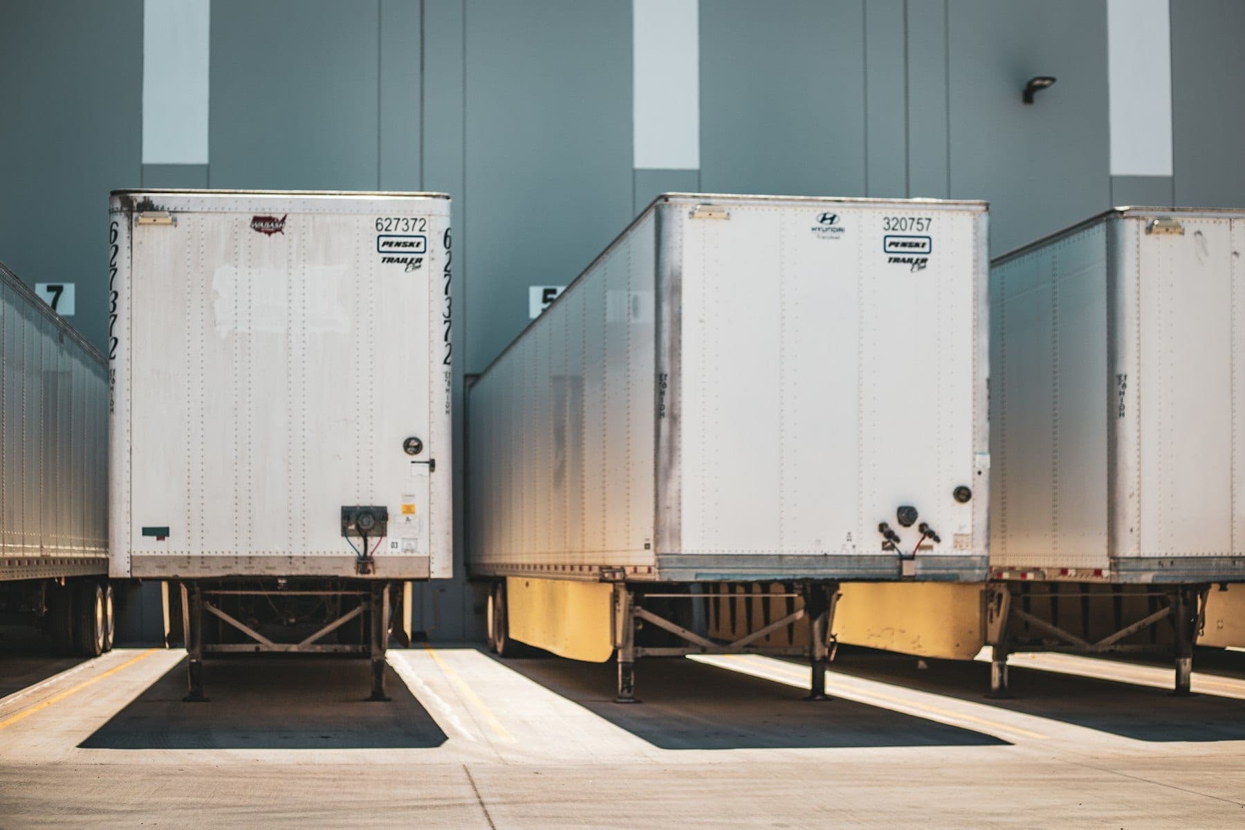 White semi trailers backed into the dock doors of a warehouse in bright sunlight