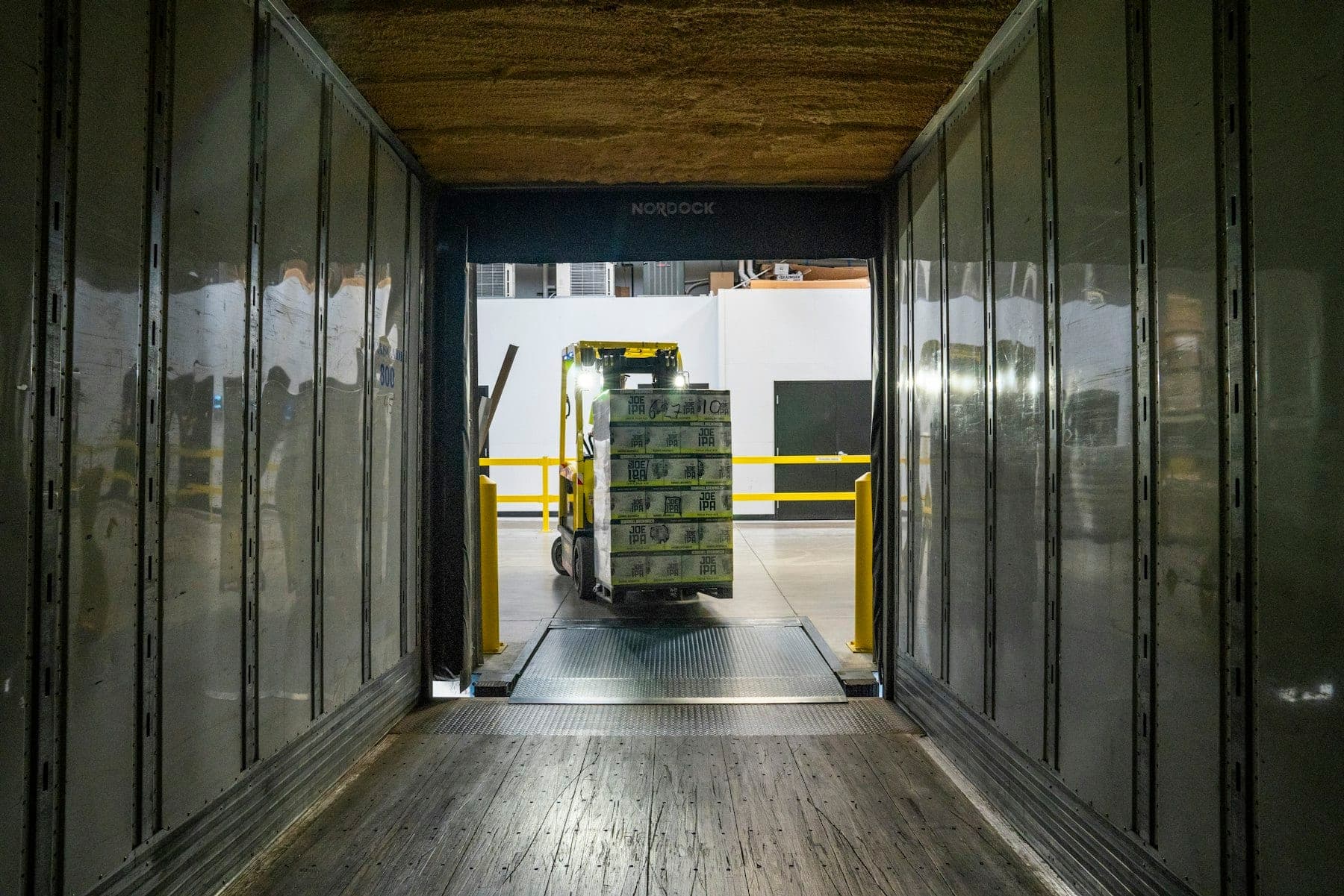 View from inside a trailer at a loading dock as a forklift brings in a shrink-wrapped pallet